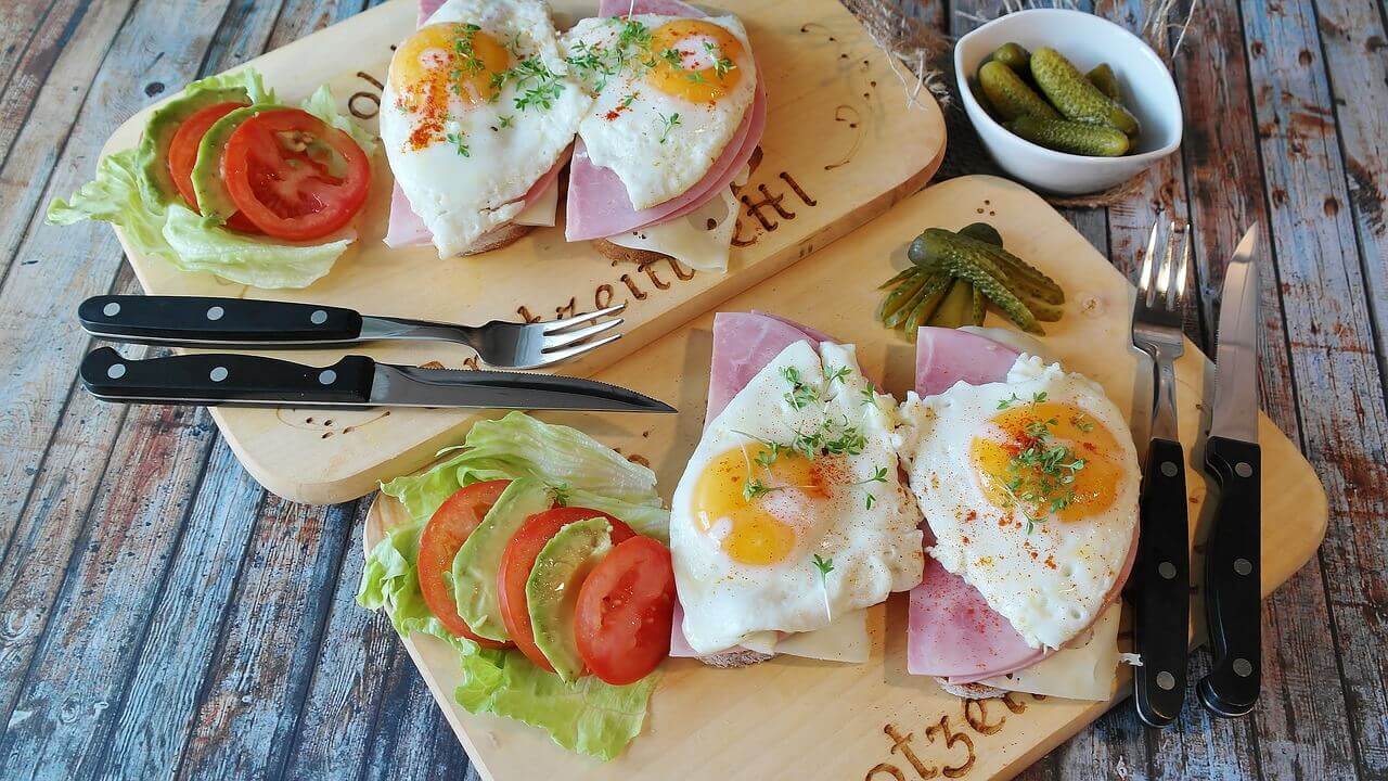 A couple of sandwiches on wooden plates with ham and eggs.