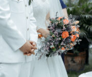 A bride and groom holding hands with their bouquet.