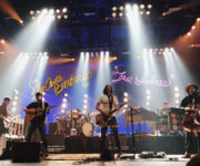 A band performing on stage with lights in the background.