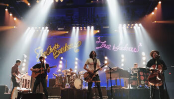 A band performing on stage with lights in the background.