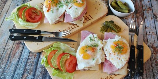 A couple of sandwiches on wooden plates with ham and eggs.